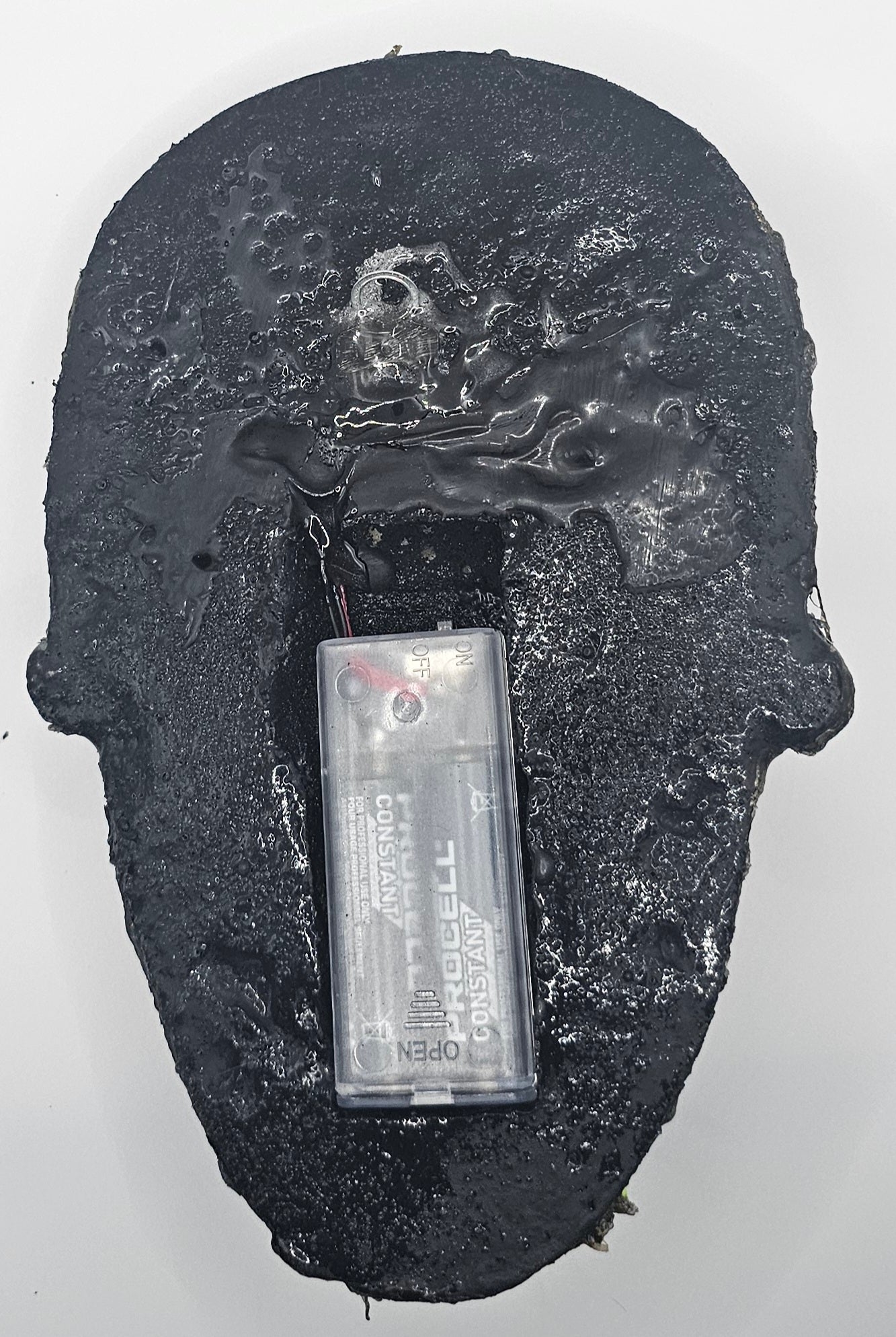 Black textured object with a small rectangular Battery pack component .