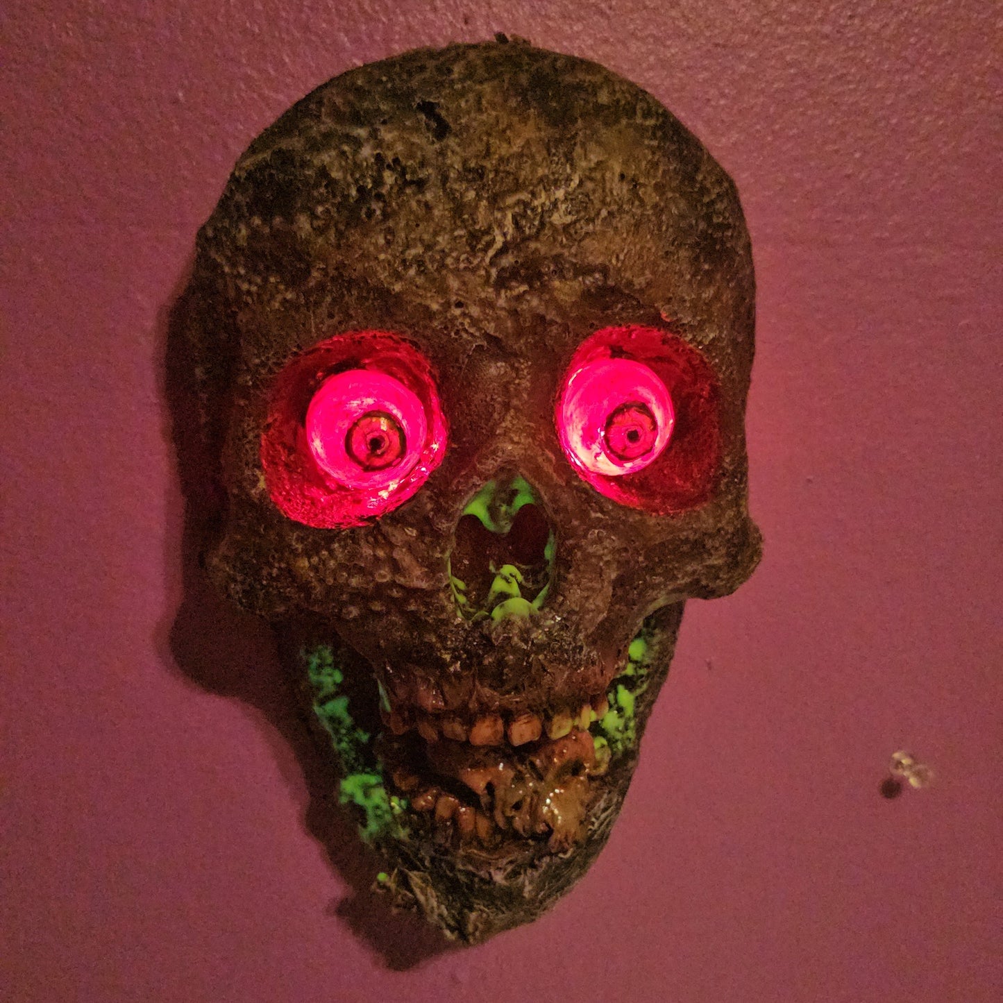 Decorative skull with glowing pink eyes on a textured pink surface