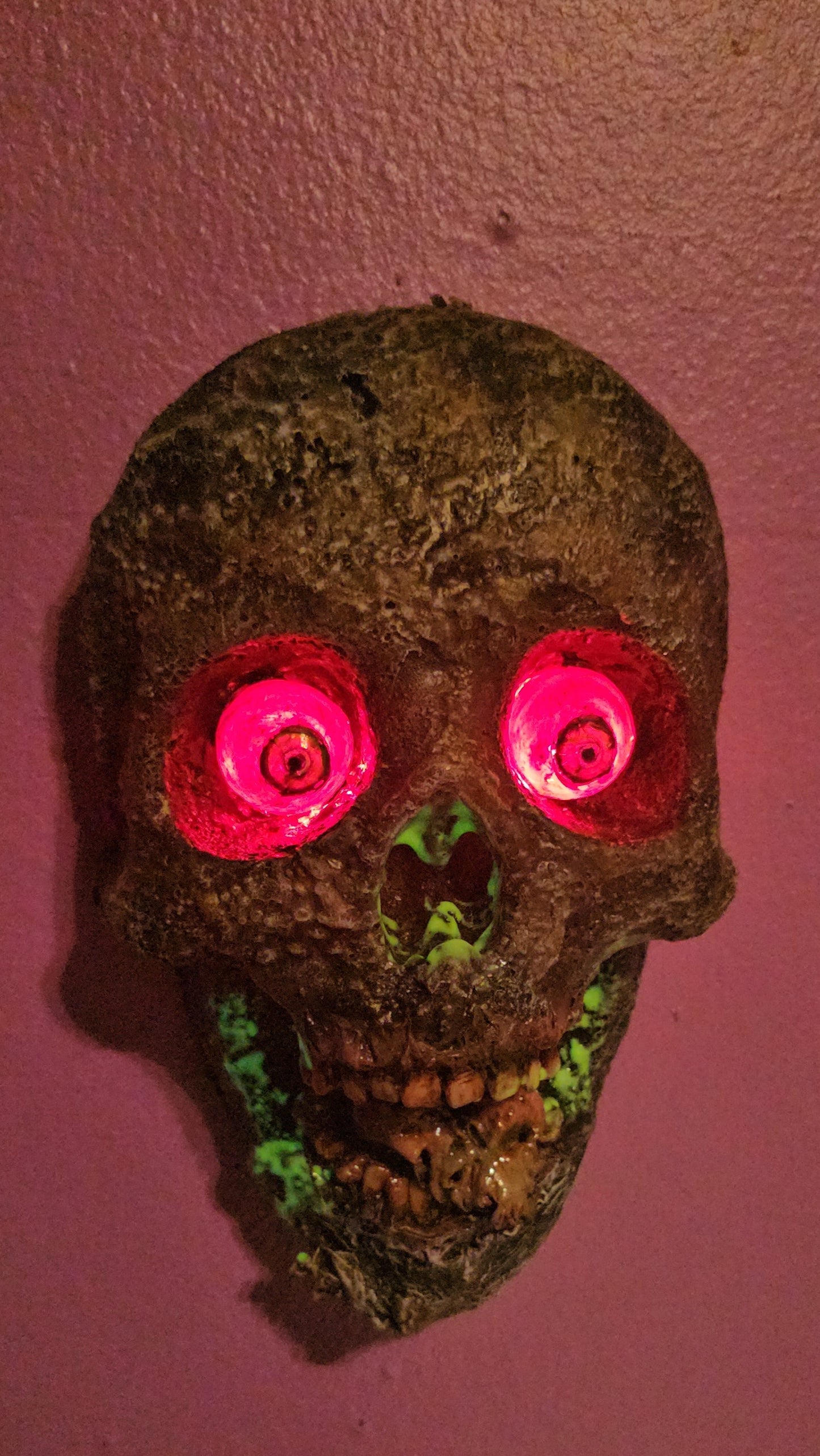 Decorative skull with glowing pink eyes on a wall,