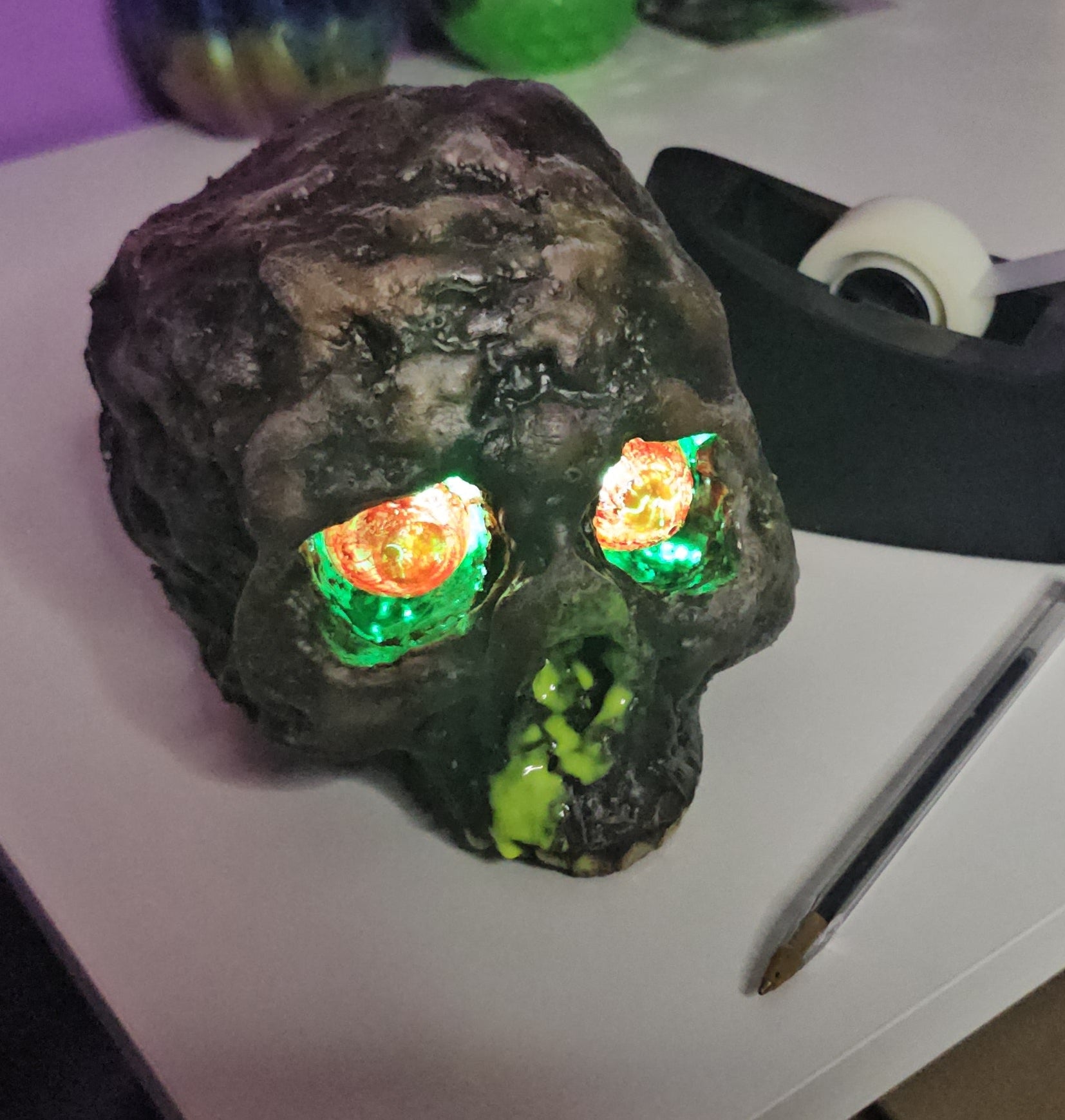 Decorative skull with glowing eyes on a table next to a tape dispenser.